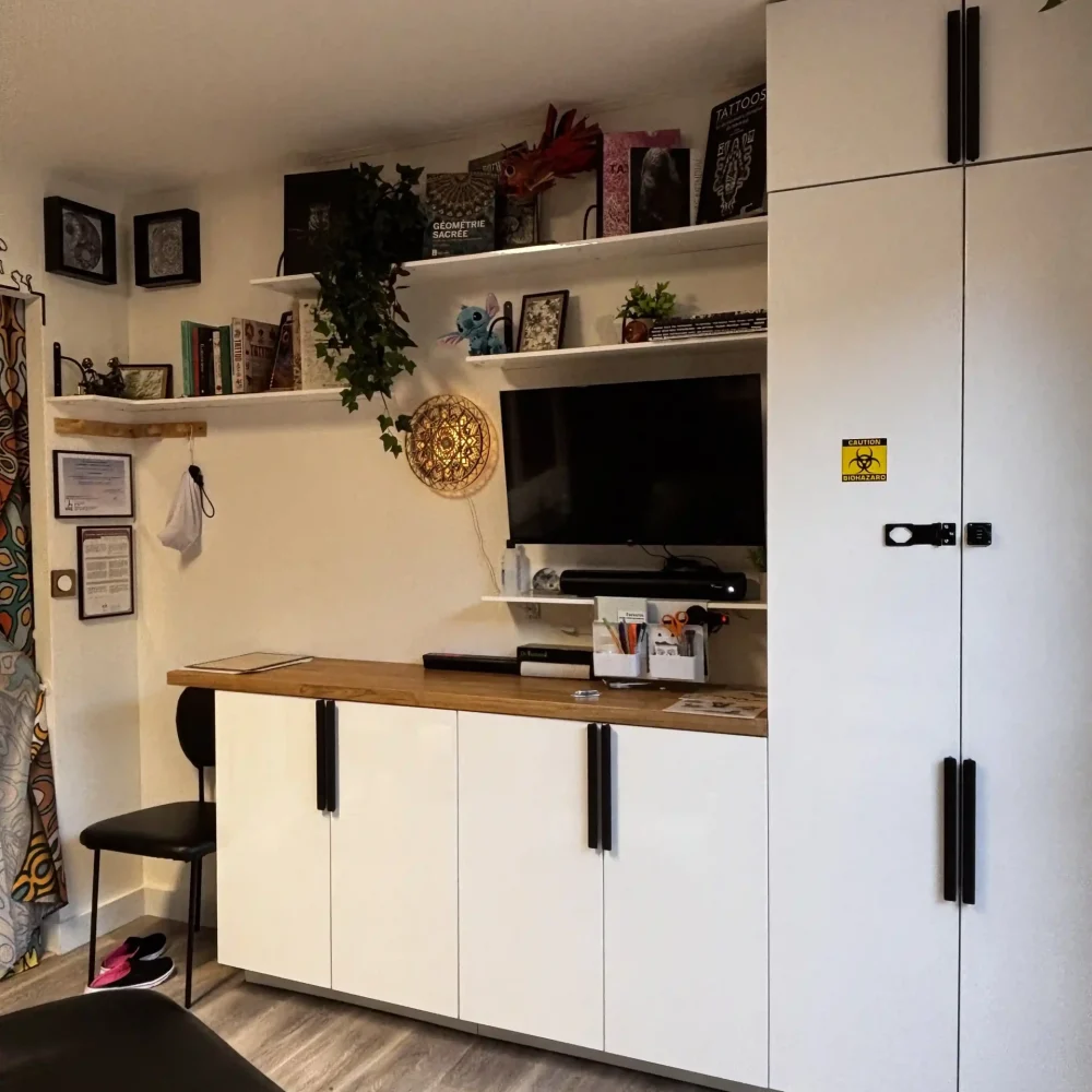 Espace de travail du studio de tatouage La Griffe avec bibliothèque de références artistiques, plan de travail en bois et mandala lumineux néon